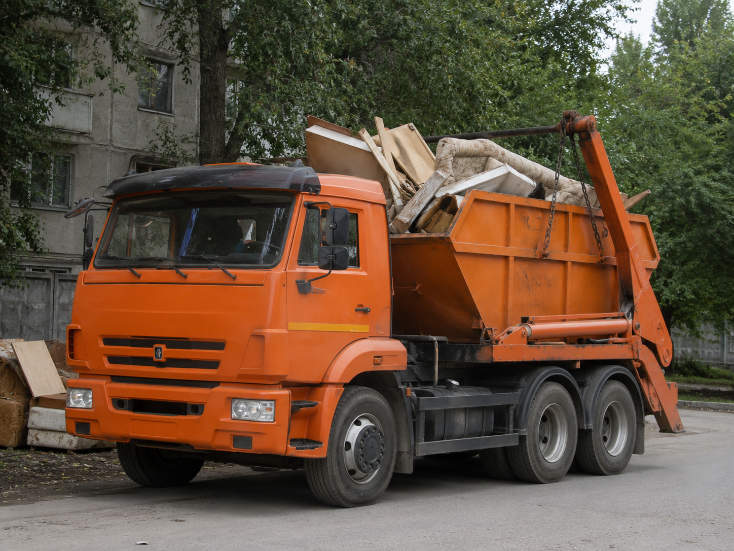 КамАЗ для вывоза крупногабаритного мусора с загруженным контейнером во дворе жилого района